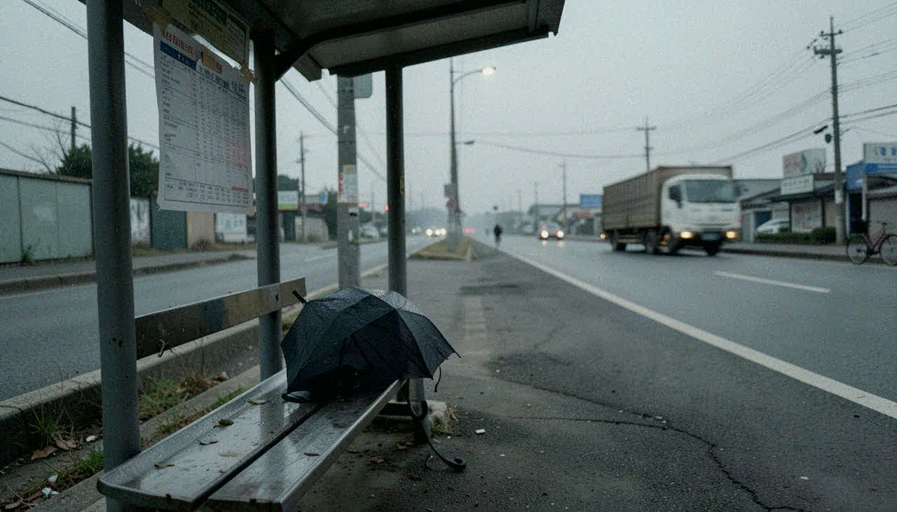 빈 정류장. 벤치의 우산 하나. 반쯤 뜯긴 시간표.