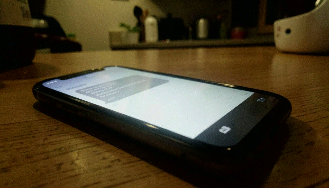 식탁 위의 휴대전화. 통보 문자 화면. 조명 반사로 내용 판독 불가.